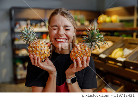 A Joyful Woman Excitedly Holding Fresh and Ripe Pineapples Inside a Vibrant Grocery Store 119712421