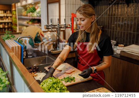 A young woman diligently preparing fresh, vibrant ingredients in her lively kitchen environment 119712455