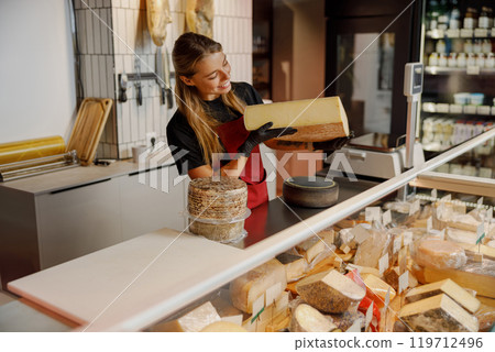 Cheese Shop Worker Skillfully Handling a Diverse Range of Artisan Cheeses for Customers 119712496