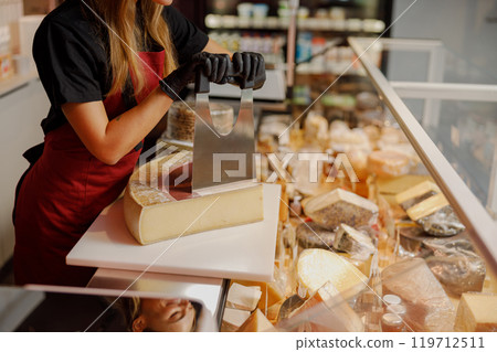 Cheese seller skillfully preparing a variety of delicious cheese in a specialty store Cheese seller skillfully preparing a variety of delicious cheese in a specialty store 119712511