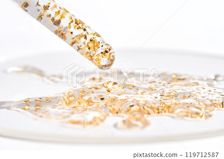 Luxurious golden serum with gold flakes in dropper on a glass surface Luxurious golden serum with gold flakes in dropper on a glass surface 119712587