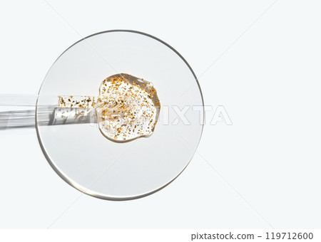 Close-up of liquid with gold particles in petri dish on white background 119712600