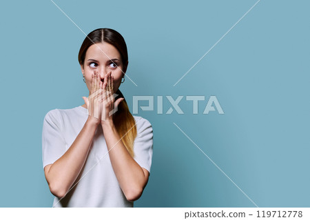 Surprised beautiful young woman covering her open mouth with her hands, on blue background Surprised beautiful young woman covering her open mouth with her hands, on blue background 119712778