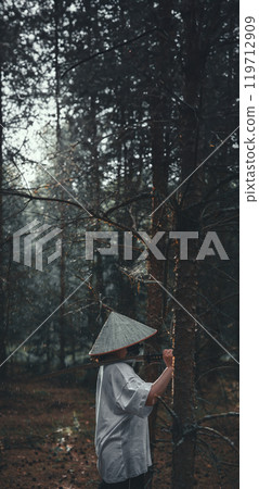 A young man in the forest, wearing an Asian hat and holding a katana, practices martial arts in the rain, conveying the essence of Japanese warrior culture. Samurai with a katana. 119712909