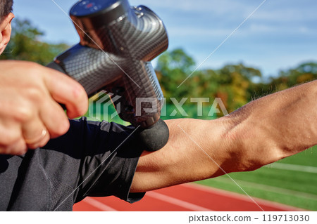 Athlete using handheld massage gun on arm after workout 119713030
