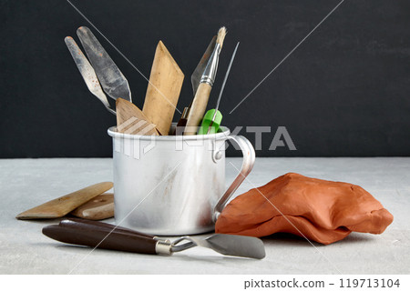 tools for modeling and sculpting and pieces of clay and plasticine on a stone table in a sculptor's workshop against a black wall 119713104