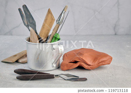 mug with many tools for sculpting and modeling and pieces of clay and plasticine on a stone table of a sculptor's workshop 119713118