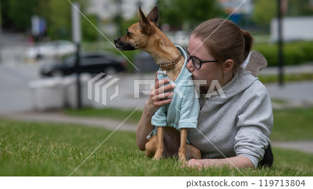 Young Caucasian woman lying on the lawn while walking with a small dog. Young Caucasian woman lying on the lawn while walking with a small dog. 119713804