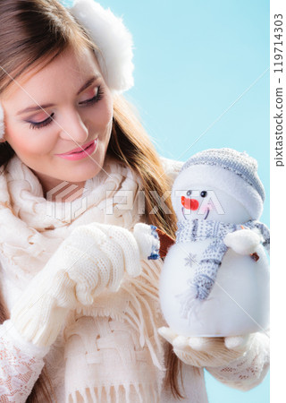 Woman in warm clothes holding snowman toy. 119714303