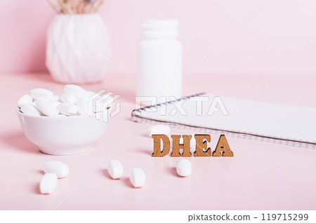 Hormonal supplement DHEA in tablets and a notebook on the table 119715299