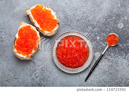 Small metal plate with red salmon caviar and two caviar toasts canape top view on grey concrete background, festive luxury delicacy and appetizer 119715591