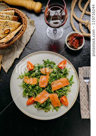 Gourmet arugula salad with smoked salmon and cherry tomatoes, served with red wine and rustic bread 119716244