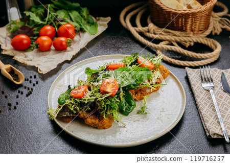 Crispy chicken cutlets topped with fresh greens, cherry tomatoes, and Parmesan 119716257
