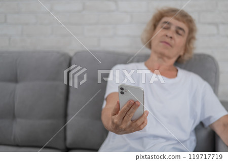An elderly Caucasian woman suffers from farsightedness and tries to read a message on a smartphone with her arm outstretched.  119717719