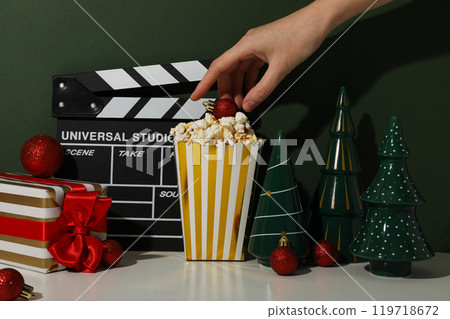 Clapperboard, paper cup with popcorn, hand and Christmas decorations on green background 119718672