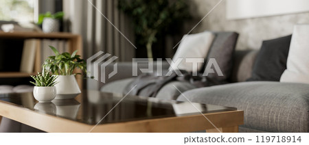 A close-up of a coffee table in a contemporary living room featuring a comfortable grey sofa. 119718914