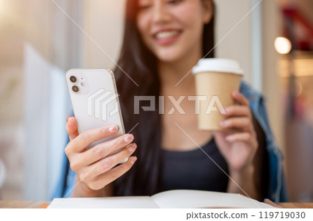 A close-up of a woman reading text messages on her smartphone while enjoying coffee in a coffee shop A close-up of a woman reading text messages on her smartphone while enjoying coffee in a coffee shop 119719030