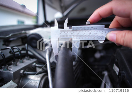 Close up of vernier caliper measuring rubber tube of engine component 119719116