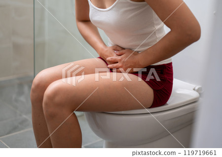 A woman sitting on a toilet, gently touching her stomach, severe stomach pain or period cramps. A woman sitting on a toilet, gently touching her stomach, severe stomach pain or period cramps. 119719661