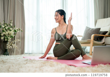 A fit, healthy Asian woman in sportswear is practicing yoga at home from an online tutorial. 119719758