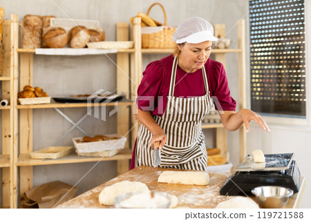 Woman baker cuts and weighs pieces of dough Woman baker cuts and weighs pieces of dough 119721588
