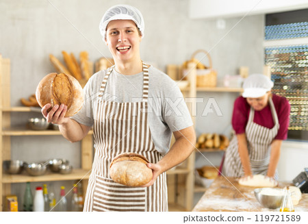 Happy young guy baker posing with basket of freshly baked bread in bakery Happy young guy baker posing with basket of freshly baked bread in bakery 119721589