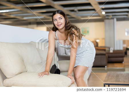 Young woman carefully examines sofa before buying and checks elasticity of surface with hand 119721694