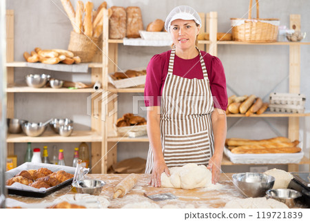 Adult female baker kneading dough on table Adult female baker kneading dough on table 119721839