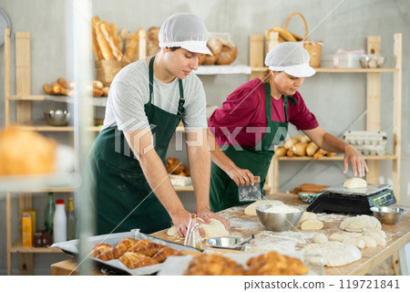Male and female bakers knead dough, cut and weigh pieces Male and female bakers knead dough, cut and weigh pieces 119721841