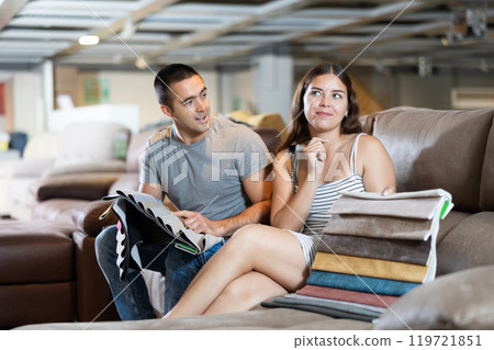 In exhibition hall,couple sat down on brown sofa and keep sets of upholstery material samples In exhibition hall,couple sat down on brown sofa and keep sets of upholstery material samples 119721851
