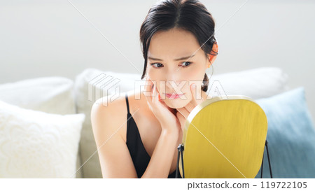 A woman checking her skin in the mirror indoors A woman checking her skin in the mirror indoors 119722105