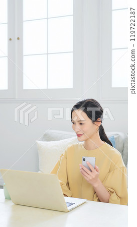 Woman using smartphone and laptop in living room 119722187