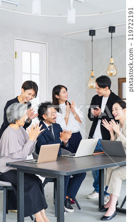 A group of business people of all ages clapping in an office 119722191