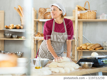Adult female baker kneading dough on table Adult female baker kneading dough on table 119722230