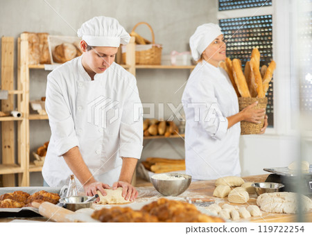 Male baker stands at his work bench, kneading and shaping dough to make bread, croissants and baguettes Male baker stands at his work bench, kneading and shaping dough to make bread, croissants and baguettes 119722254