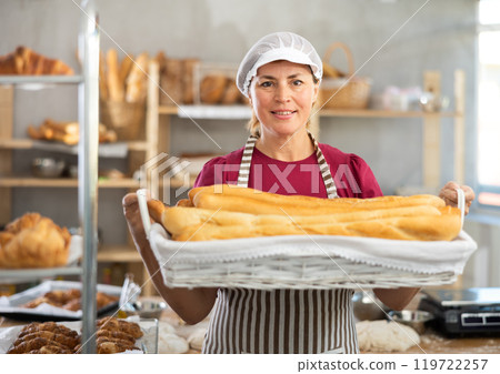 Adult female baker with basket of baguettes 119722257