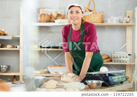 Adult female baker kneading dough on table 119722285