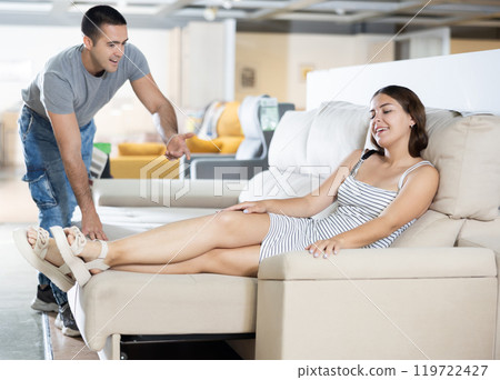 Couple chooses furniture in store.Wife is sitting on sofa,husband is standing next to her 119722427