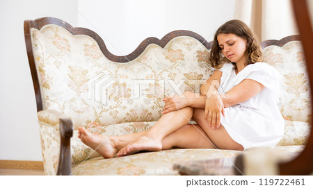 Smiling young woman in white dress posing on couch at home Smiling young woman in white dress posing on couch at home 119722461