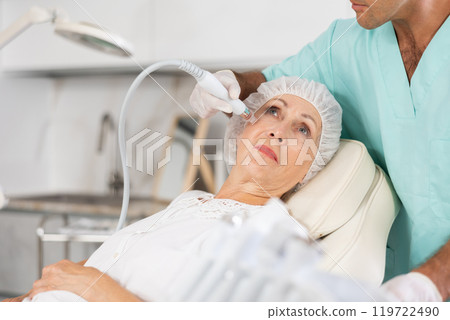Male dermatologist performing cosmetology procedure for elderly woman, RF lifting and deep hydration for facial skin therapy Male dermatologist performing cosmetology procedure for elderly woman, RF lifting and deep hydration for facial skin therapy 119722490