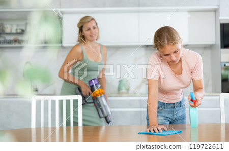 Teenage girl wiping table with rag and detergent at home kitchen 119722611