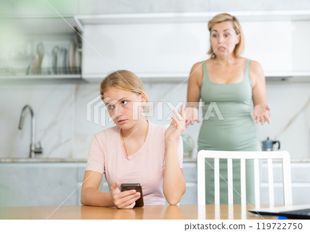 Teenage girl with smartphone making dismissive gesture to mother Teenage girl with smartphone making dismissive gesture to mother 119722750