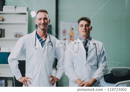 Portrait of two dedicated doctors smiling and looking at camera while holding a tablet and a diary in clinic. Two smiling doctors in white coat working in an office and looking at camera. 119723002