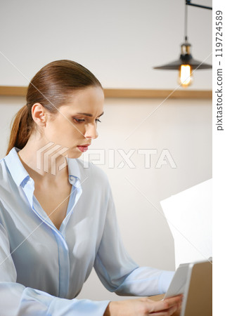 Focused woman working diligently on a document in a stylish office during the daytime Focused woman working diligently on a document in a stylish office during the daytime 119724589