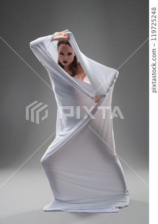 Woman in a flowing white garment performs an expressive dance in a studio 119725248