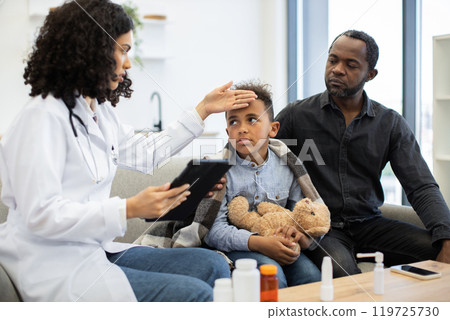 Doctor checking fever of young boy with father beside him Doctor checking fever of young boy with father beside him 119725730
