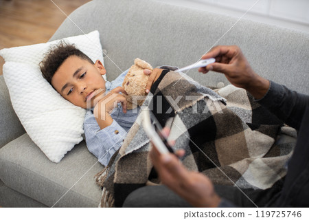 Dad takes care of sick boy with thermometer and phone consultation Dad takes care of sick boy with thermometer and phone consultation 119725746