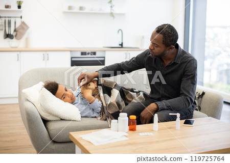 Father takes temperature of sick child in cozy home setting 119725764