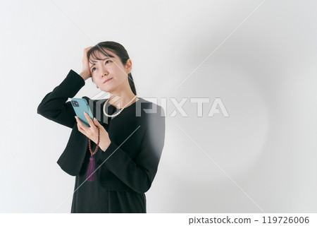 A woman in mourning clothes thinking with her smartphone 119726006