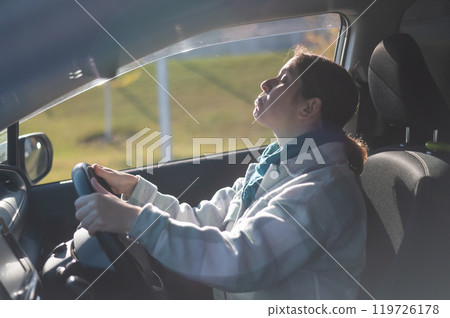Caucasian woman sitting behind the wheel and looking in the mirror.  119726178